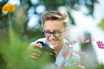 Funny boy teenager 15 years old with a camera takes pictures in the park in summer