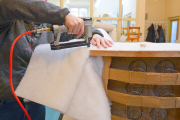 Making new upholstery on old armchair. Woman hands working in upholstery workshop with pneumatic...