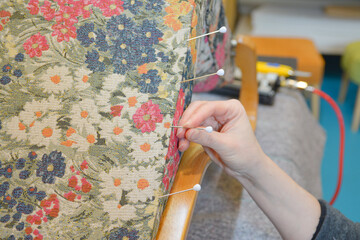 Woman hands sewing with upholstery round needle. Upholsterer working with fabric with flowers...