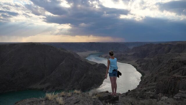 A girl stands at the edge of a canyon on a windy day. Great view of the canyon with the river. Slow motion