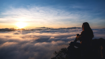 Obraz premium A female traveler sitting on the mountain peak, watching sunrise and sea of fog