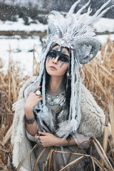 beautiful woman with black hair and fantasy make-up, in crown with braids, horns and feathers, in...