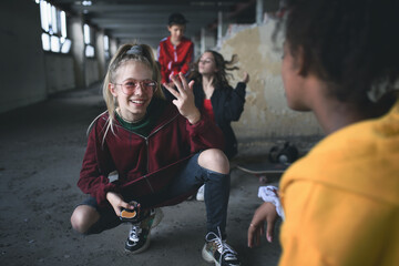 Group of teenagers gang sitting indoors in abandoned building, using smartphones.