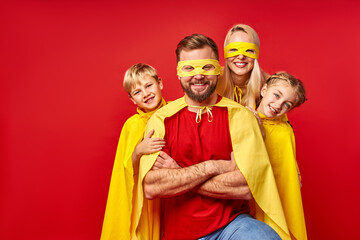 cute mother and kis hide behind a super man's back wearing yellow cloaks and masks, costume of...