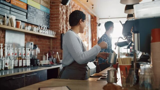 Beautiful Latin American Female Barista with Short Hair and Glasses is Making a Cup of Tasty Cappuccino in Coffee Shop Bar. Portrait of Happy Employee Behind Cozy Loft-Style Cafe Counter.