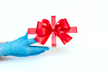 Holiday gift.Hands wearing meidical gloves holding gift box with red ribbon.white background.COVID-19 prevention.