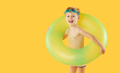Portrait of smiling happy child boy in swimming goggles with neon inflatable rubber circle having fun isolated on yellow background. Summer vacation6 funny face