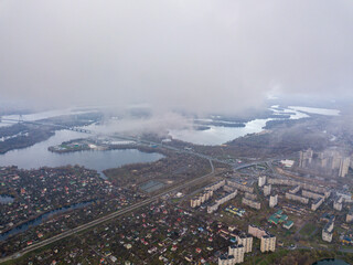 High aerial flight in the clouds over Kiev. An autumn cloudy morning, the Dnieper River is visible on the horizon.