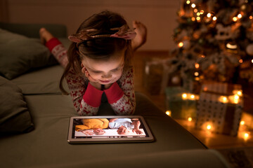 Child girl talking to grandparents by video call on tablet on Christmas Eve at home. New normal...