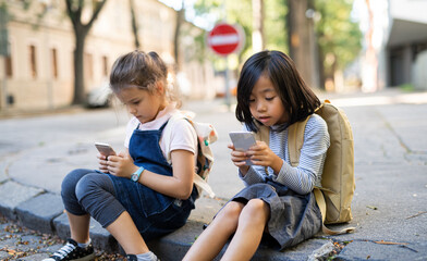 Small girls with smartphones outdoors in town, playing.