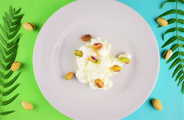 Pistachios on fresh cheese, served on a white porcelain plate. Two-color background with small natural leaves.