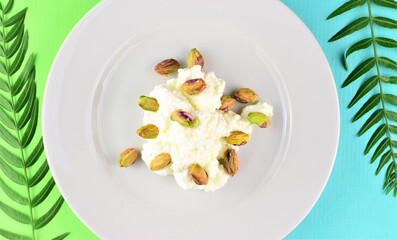 Close up. In this case pistachios on fresh cheese, served on a white porcelain plate. Two-color background with small natural leaves.