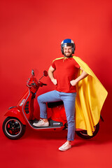 happy caucasian male is perfect driver of motorbike, stand in cloak of super hero isolated over red...