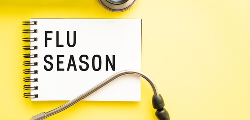 Text FLU SEASON on notebook with stethoscope on yellow background.
