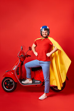 happy caucasian male is perfect driver of motorbike, stand in cloak of super hero isolated over red background