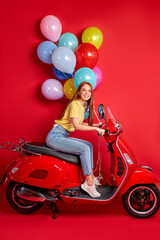 Fototapeta na wymiar portrait of redhead smiling female on motorcycle, young female delivers bright air balloons to clients, drive red bike