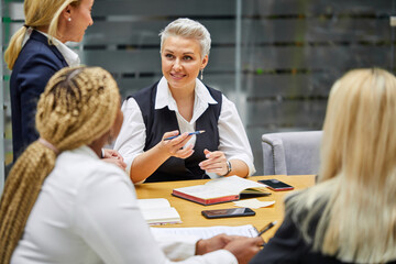 group of interracial business women listening to adult female boss, successful cooperation of colleagues, good work, they have conversation, in formal wear