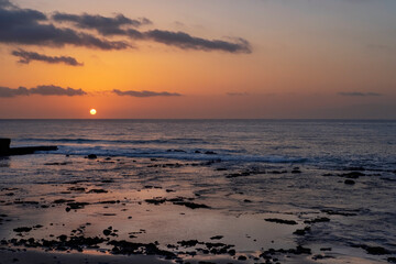 Spectacular sunset with purple hues and calm ocean waves on a wild beach near Palm Mar resort, atmospheric evening with sun dipping into the sea, crepuscular landscape, Tenerife, Canary Islands, Spain