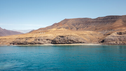 Approaching Fuerteventura island at its most southern point, at Morro Jable with the display of the solitary cliffs and arid mountains behind, part of the Parque Natural Jandia, Canary Islands, Spain