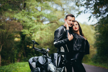 Fototapeta na wymiar Loving couple, guy and girl bikers, in black leather clothes. near a sports motorcycle on a forest road