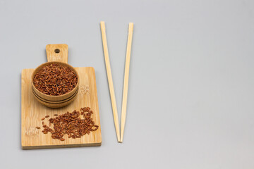 Red rice in a wooden bowl on cutting board. Bamboo sticks