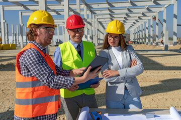 Construction Foreman in Yellow Hardhat Holding Digital Tablet and Discuss a Project With Female Architect and Businessman