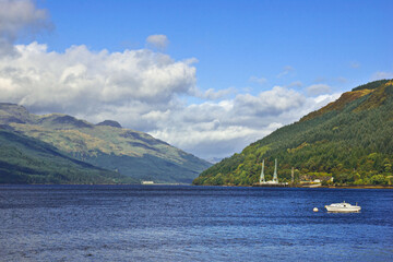 Beautiful scenery along the shores of Loch Long, Argyllshire, Scotland, where fluffy white clouds cast shadows over the mountains sweeping down to the sunlit blue waters of the lake.