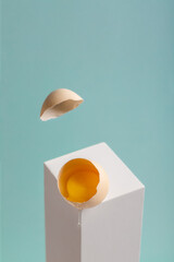 Half raw chicken egg with yolk on light blue background. Egg balanced on white pedestal.