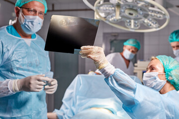 medical workers in hospital examine x-ray prints during operation, caucasian medics consult with each other while looking at x ray image, medicine, surgery, healthcare concept