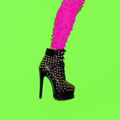 Fashion leg in heel party boots on green minimal background. Stylish clubbing mood. After party concept