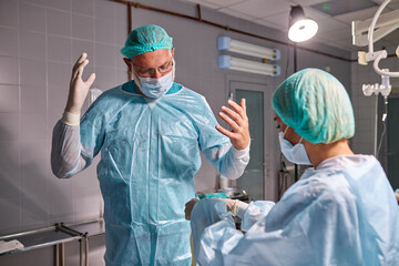 assistant preparing doctor for future surgery operation, wearing disposable medical suit on him
