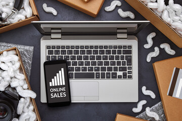 Online sales growth concept. Laptop computer and smartphone with online sales growing bar graph on screen surrounded by parcels packages boxes. Flat lay