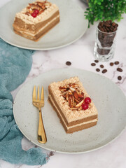 A plate of pieces of a light layered genoise sponge coffee cake topped with caramel almond with fork and coffee beans in background. It made with whole egg cake and butter 