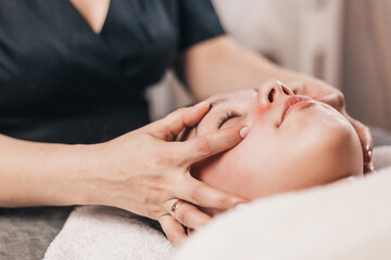 Fototapeta na wymiar Technique for performing a facial massage in a beauty salon - hands of a professional masseur - rejuvenation and relaxation of facial muscles