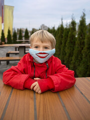 Boy in blue anti-virus mask with drawn funny smile on it . A fun DIY face mask for safety in a...