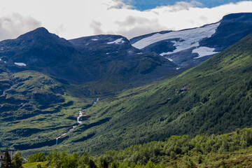 Large green mountains, with snowfields at the top and a stream that descends into the valley