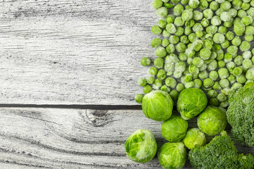 Frozen vegetables: green pea, broccoli, brussels sprout on gray wooden table. Flat lay. Horizontal orientation. Copy space.