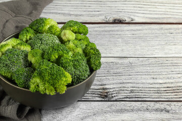 Frozen broccoli in the bowl and napkin on gray wooden table. Horizontal orientation. Copy space.