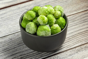Frozen brussels sprout in the bowl on gray wooden table. Horizontal orientation. Close-up.