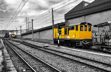 Locomotora de tren estacionado en blanco y negro con color amarillo de la locomotora resaltado - obrazy, fototapety, plakaty
