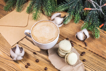 Cup of aromatic coffee and macaroons and an envelope on a wooden table on the background of a Christmas tree. Concept of a cozy atmosphere