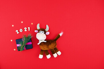 Chinese new year 2021 year of the ox. Plush toy on a red festive background with gift. The bull is a symbol of the new year 2021.
