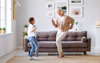 Happy grandmother dancing with granddaughter at home.