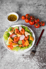 Traditional Middle Eastern vegetarian salad fattoush. Lebanese cuisine recipe. Fresh vegetables, cherry, lettuce, toasted pita bread. Gray concrete background. Low-calorie, healthy meal.