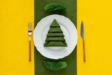 Table setting with spruce, plate, flatware on yellow background top view