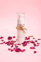 Natural herbal lotion concept. Cosmetic product bottle with rose blossom branch on a light pink background. Blank label for branding mock-up, copy space.