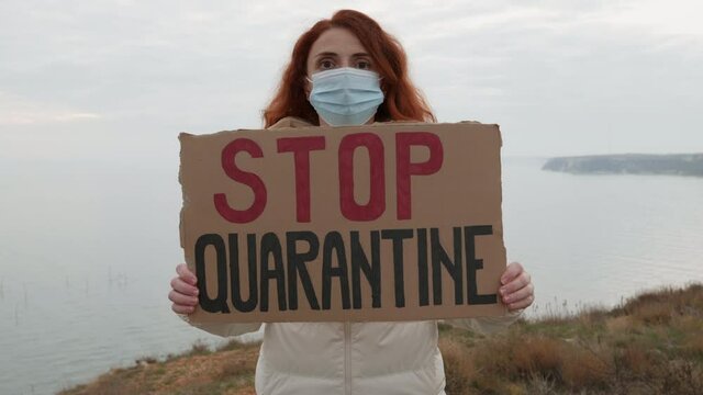 Stop Quarantine woman protest holds hands cardboard with sign Game Over in covid-19 medical mask against background blue sunset sky in evening in winter. Quarantine. Lockdown. Coronavirus. Epidemic