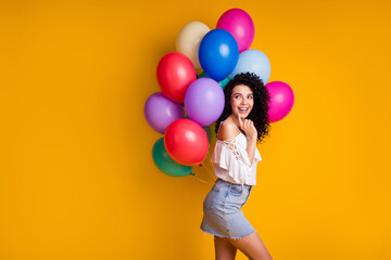 Fototapeta na wymiar Profile photo of funny brown curly girl hold many balloons behind back look empty face wear top skirt isolated on yellow background