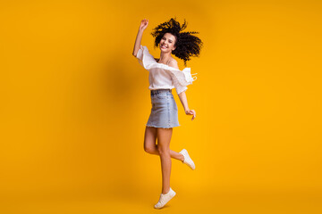 Fototapeta na wymiar Full size photo of funny optimistic brunette curly woman dancing wear white top blue skirt sneakers isolated on yellow color background