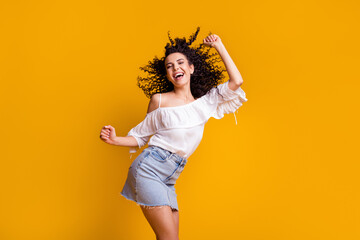 Fototapeta na wymiar Photo of young cheerful cute curly brunette woman dancing wearing white top blue skirt isolated on vivid yellow colored background